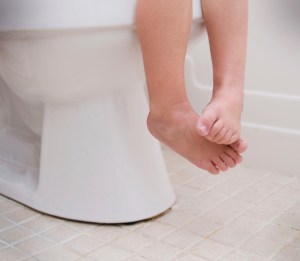Cute child feet dangling from sitting on a toilet