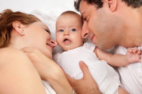Loving parents with their cute little girl lying on bed