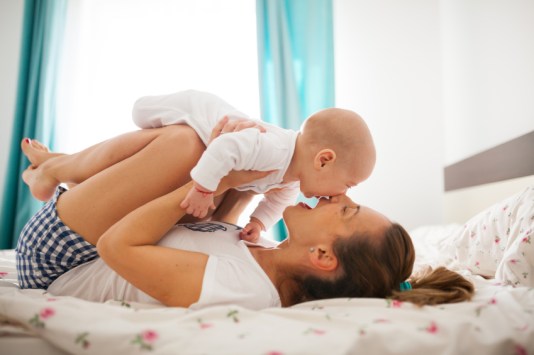 Young mother is playing with her baby boy in bed