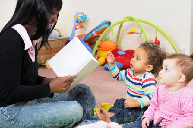 two one year old infants in child care listening to provider reading a book