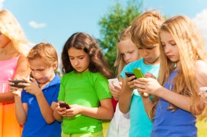 Group of busy kids looking at their phones texting sms and playing staying outside