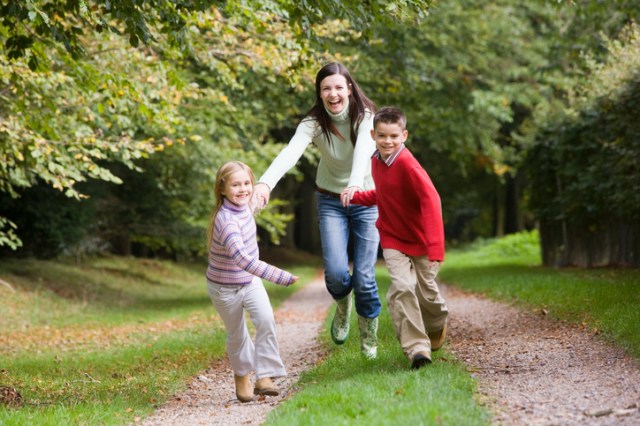 Mother and children running along woodland path in autumn