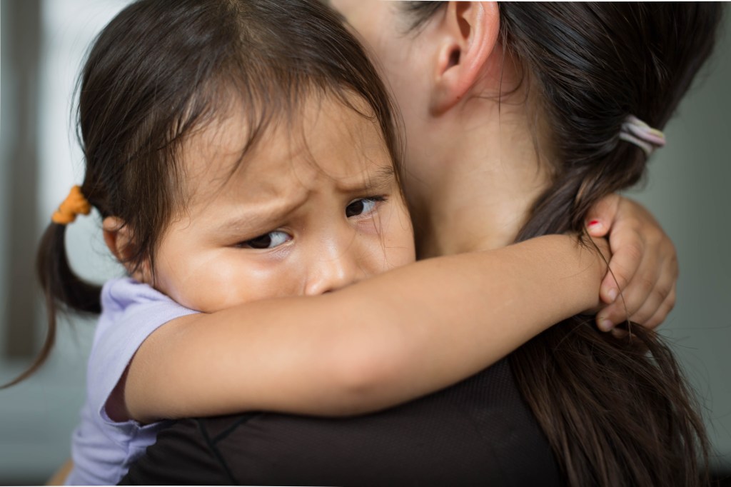 Young girl looking scared hugging her mom.