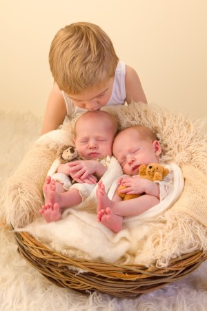 Toddler boy posing with his newborn identical twin sisters