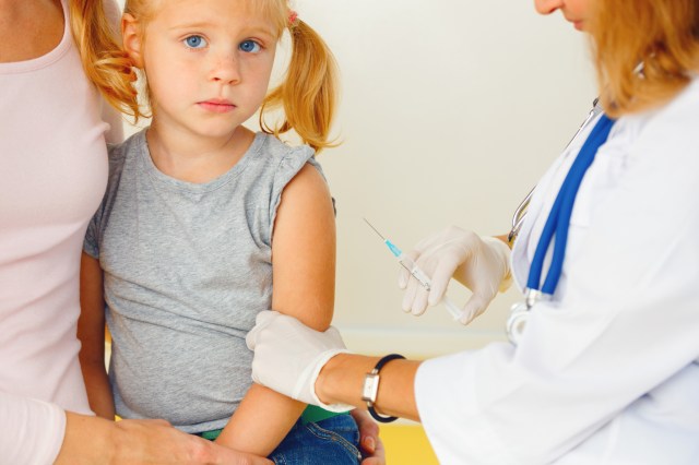 Doctor vaccinating young girl who looks afraid.