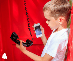 Boy in phone booth holding landline corded phone and cell phone to compare