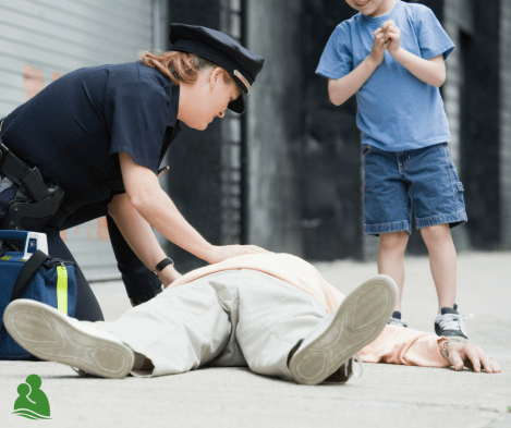 Person laying on ground with police officer looking over and young boy standing