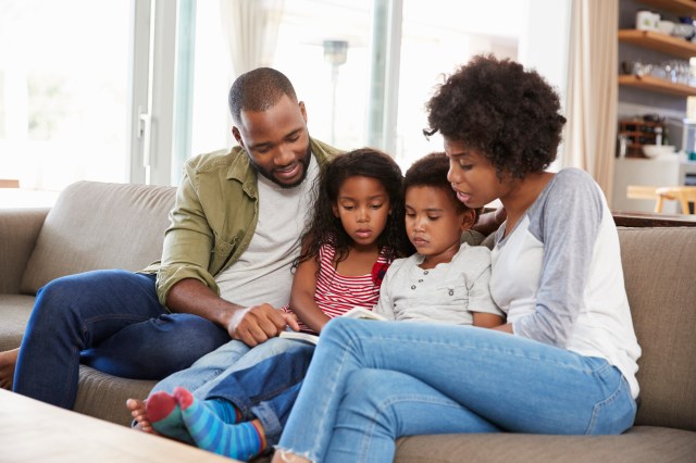 Family Sitting On Sofa In Lounge Reading Book Together