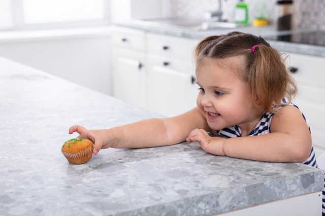 Girl's Hand Reaching For Cupcake On Kitchen Counter