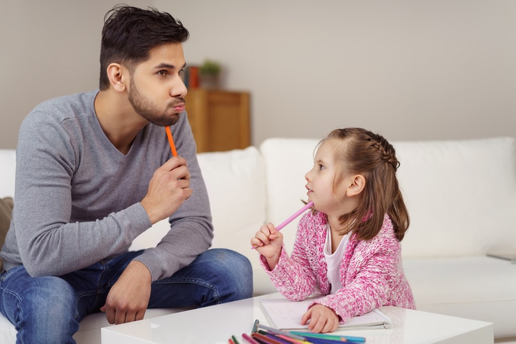 Young daughter mimicking dad both holding pencils to chins in contemplation.