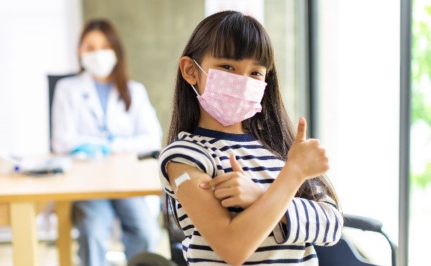 Girl wearing mask, got vaccine, thumbs up.
